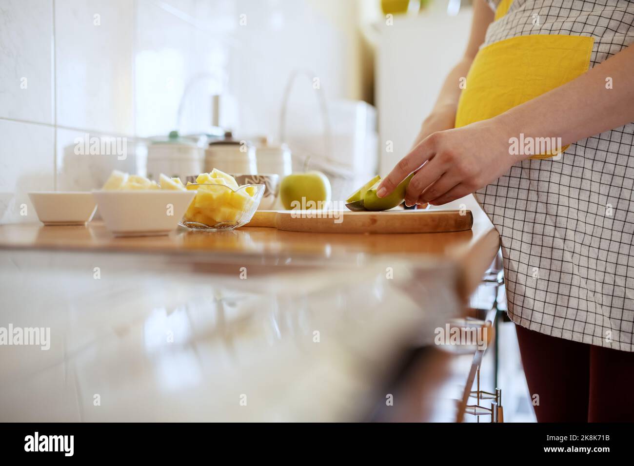 Close up of pregnant Caucasian woman in apron cutting green apple in kitchen. Stock Photo