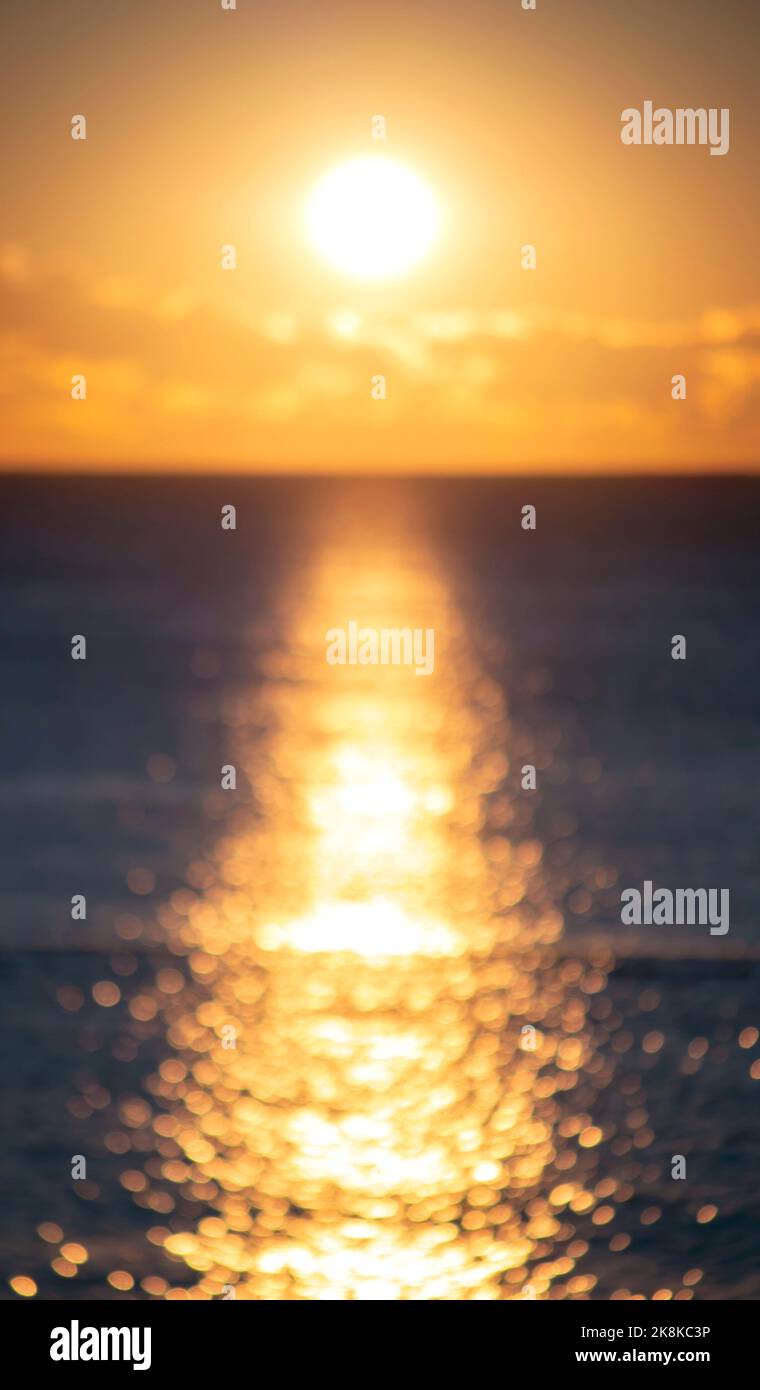 Blurred background. Sun shining in sky with clouds during sunset dawn. Sunrise dawning sundown. Sunny path, sunny walkway on surface of sea waves. Sunlight. Sea landscape. Natural blurry bokeh texture Stock Photo