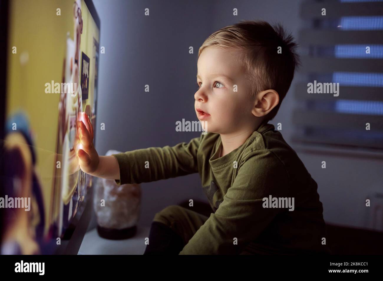 Children's addiction to television and cartoons. A boy touches the TV screen with one hand. Close up of a kid sitting right in front of the TV in his Stock Photo