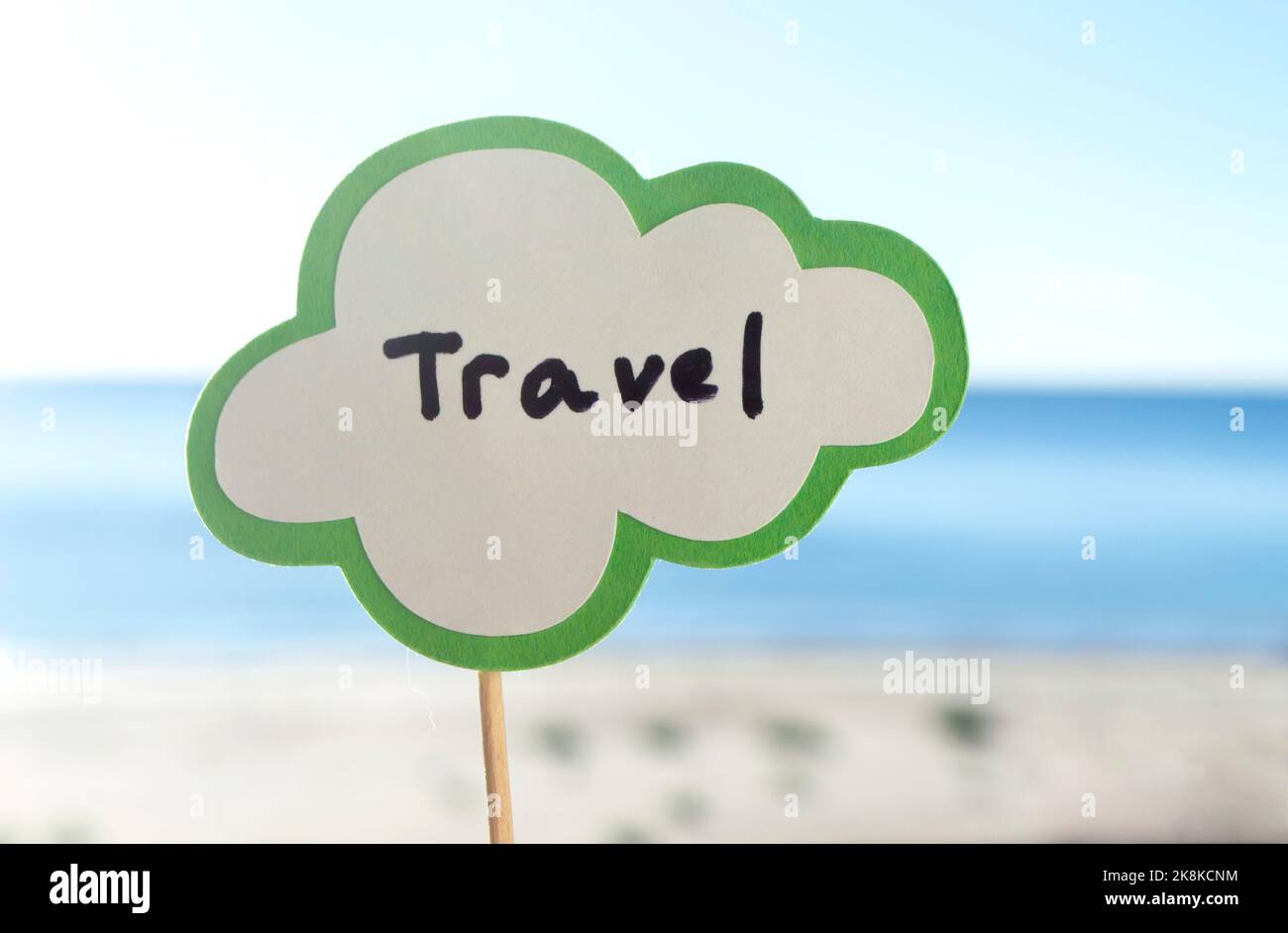 Stick with paper speech bubble with words Travel on background blue sea, sky, sandy beach on sunny summer day. Text-balloons with text from letters. Concept, symbol, sign vacation travel tourism rest Stock Photo