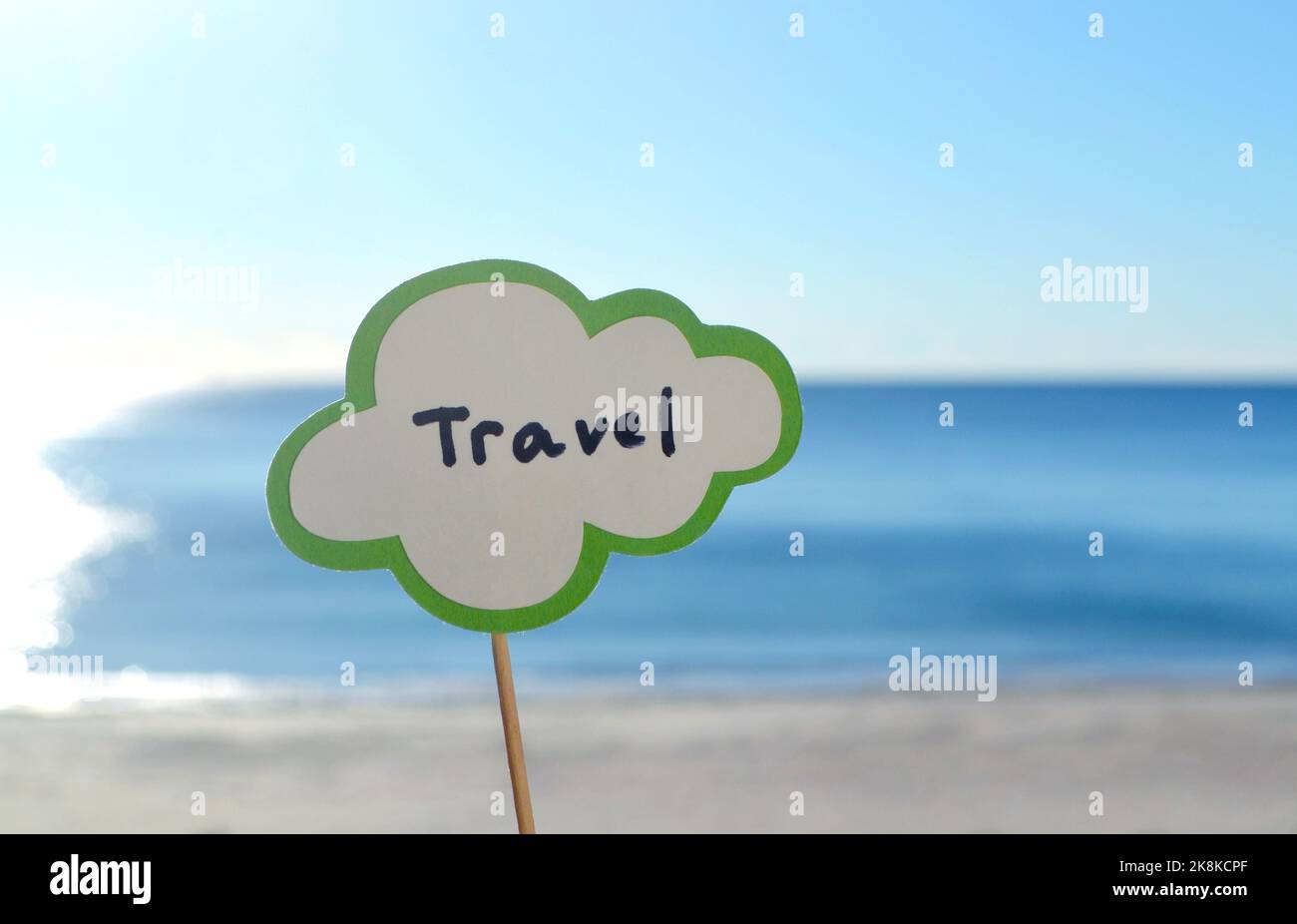 Stick with paper speech bubble with words Travel on background blue sea, sky, sandy beach on sunny summer day. Text-balloons with text from letters. Concept, symbol, sign vacation travel tourism rest Stock Photo