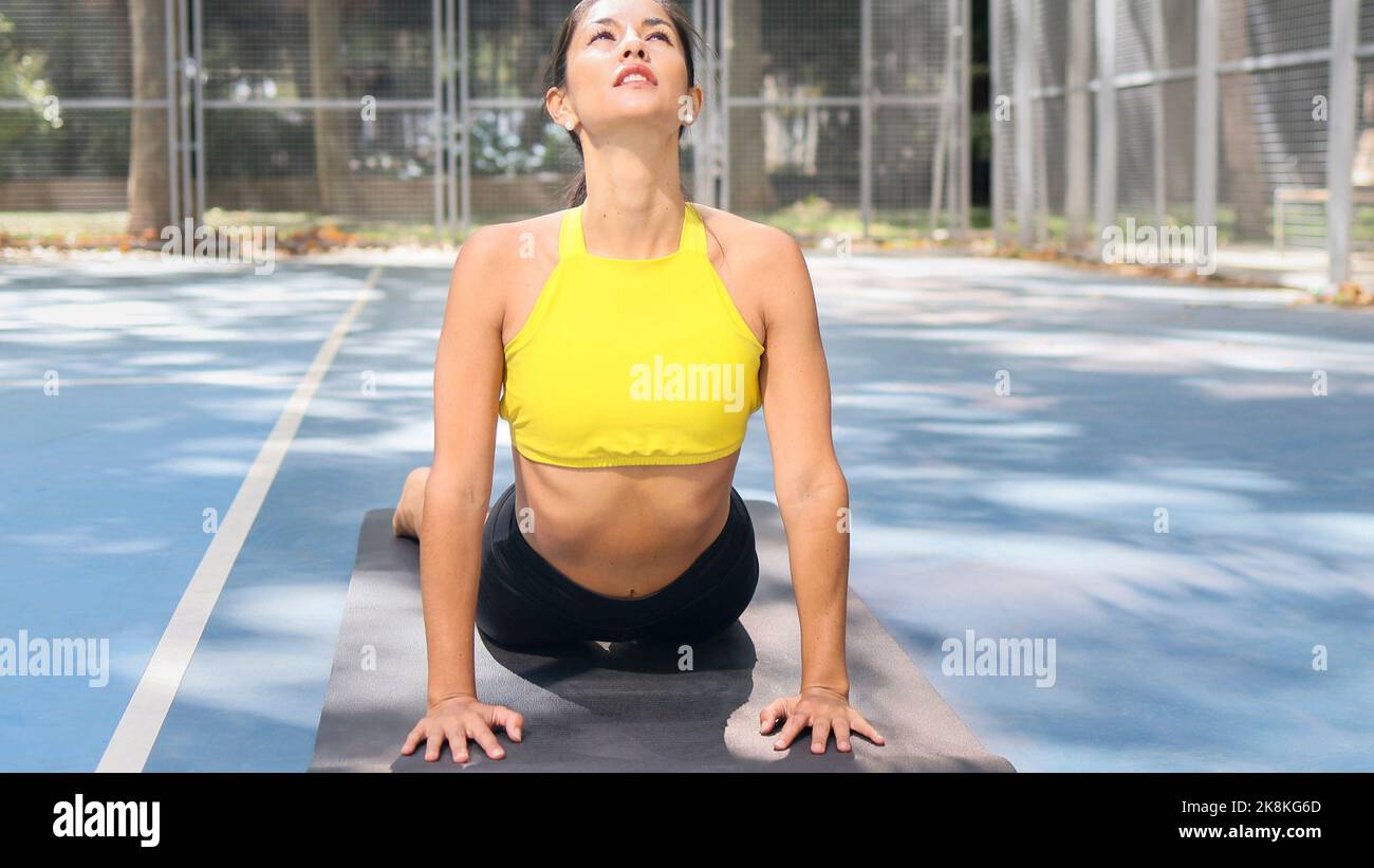 Beautiful Latin woman dressed in sports doing cobra pose outdoors. Healthcare with yoga therapy concept.  Stock Photo