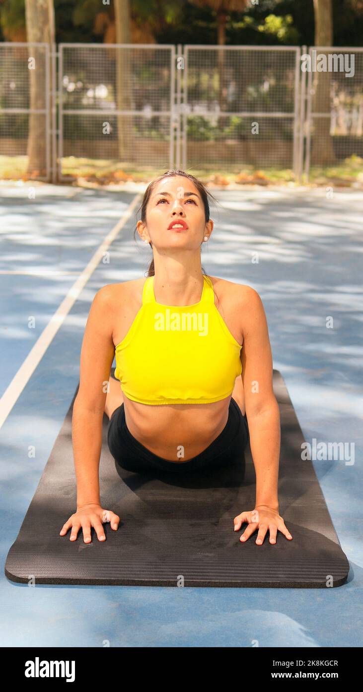 Beautiful Latin woman dressed in sports doing cobra pose outdoors. Healthcare with yoga therapy concept.  Stock Photo