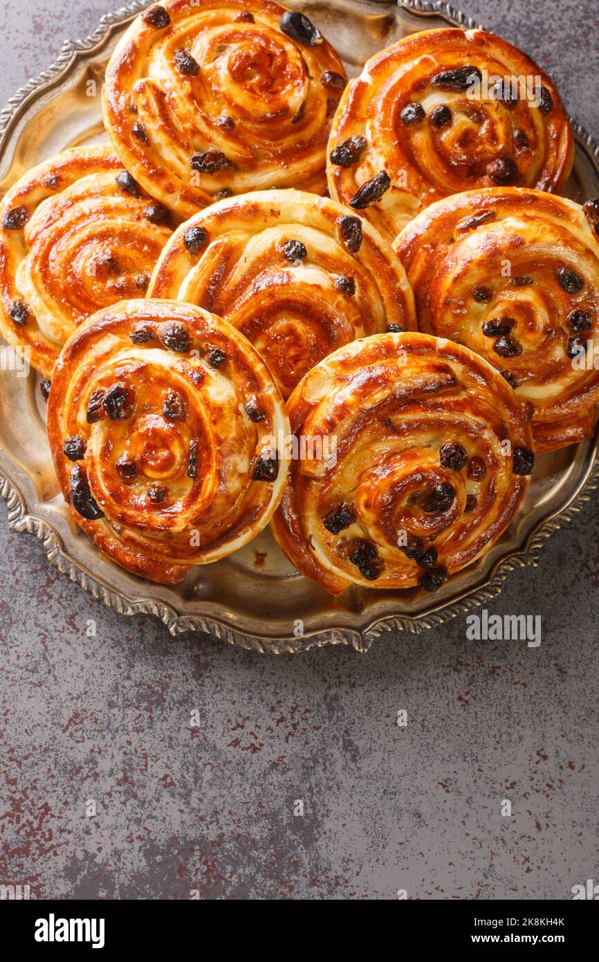 Just baked pain aux raisins buns are also called escargot or pain russe, is a spiral pastry with custard cream and raisin closeup in the plate on the Stock Photo