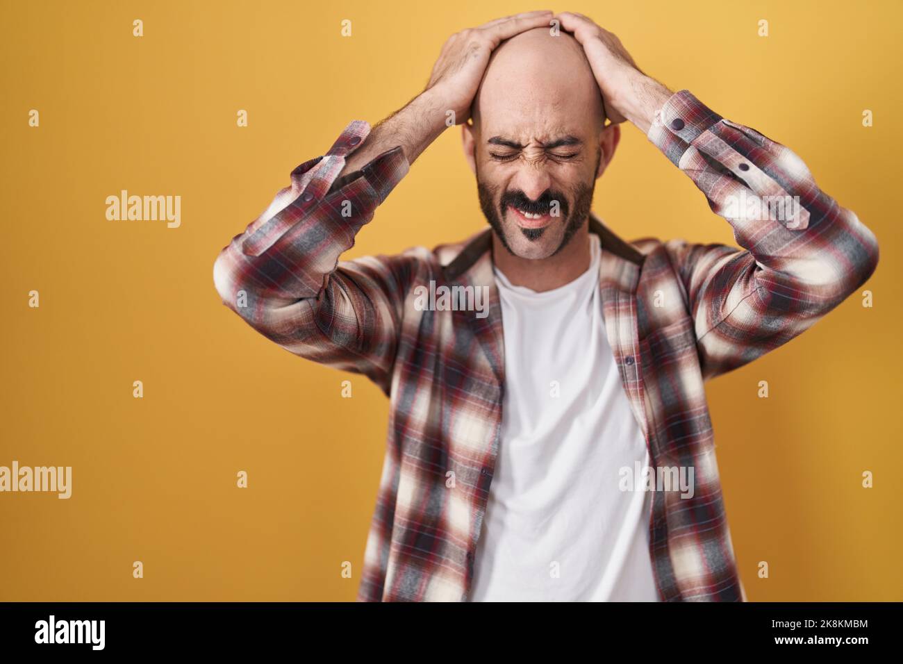 Hispanic man with beard standing over yellow background suffering from ...