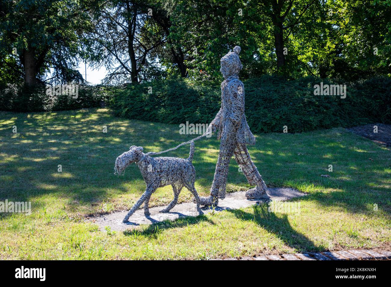 A wire sculpture of a dog walker on a roundabout in Rugby Stock Photo