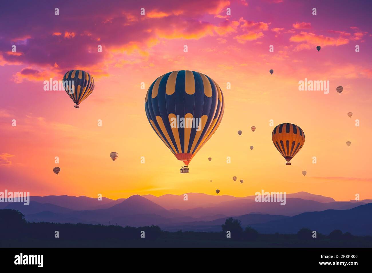 Amazing pink orange sunrise with colorful hot air balloons over spectacular mountain range in morning fog. Background for your travel concept. Natural summer scenery, morning sun rise watching Stock Photo