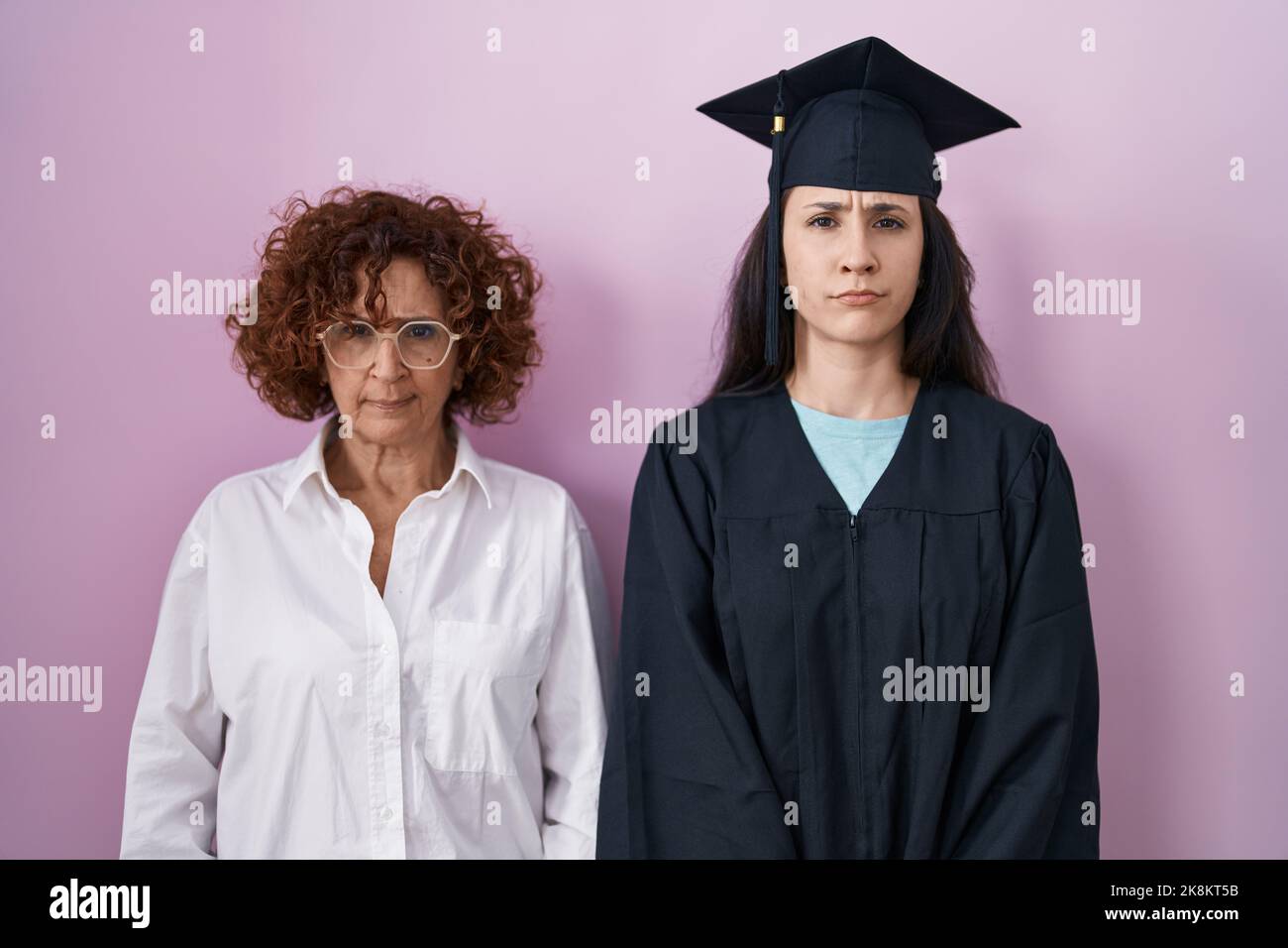 Hispanic mother and daughter wearing graduation cap and ceremony robe skeptic and nervous, frowning upset because of problem. negative person. Stock Photo