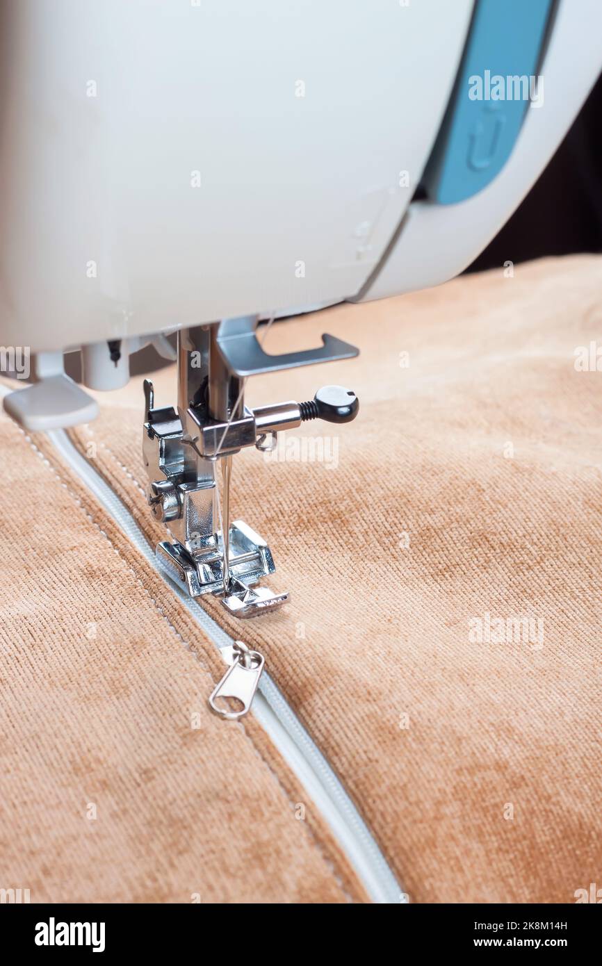Modern sewing machine sews on the zipper on biege item of clothing