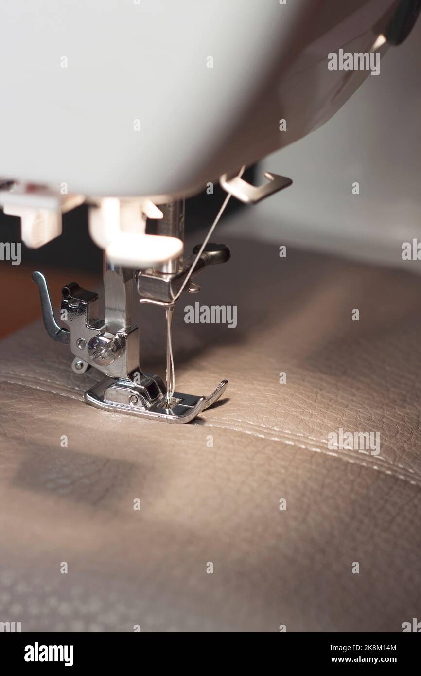 Modern sewing machine with special presser foot makes a seam on grey ...