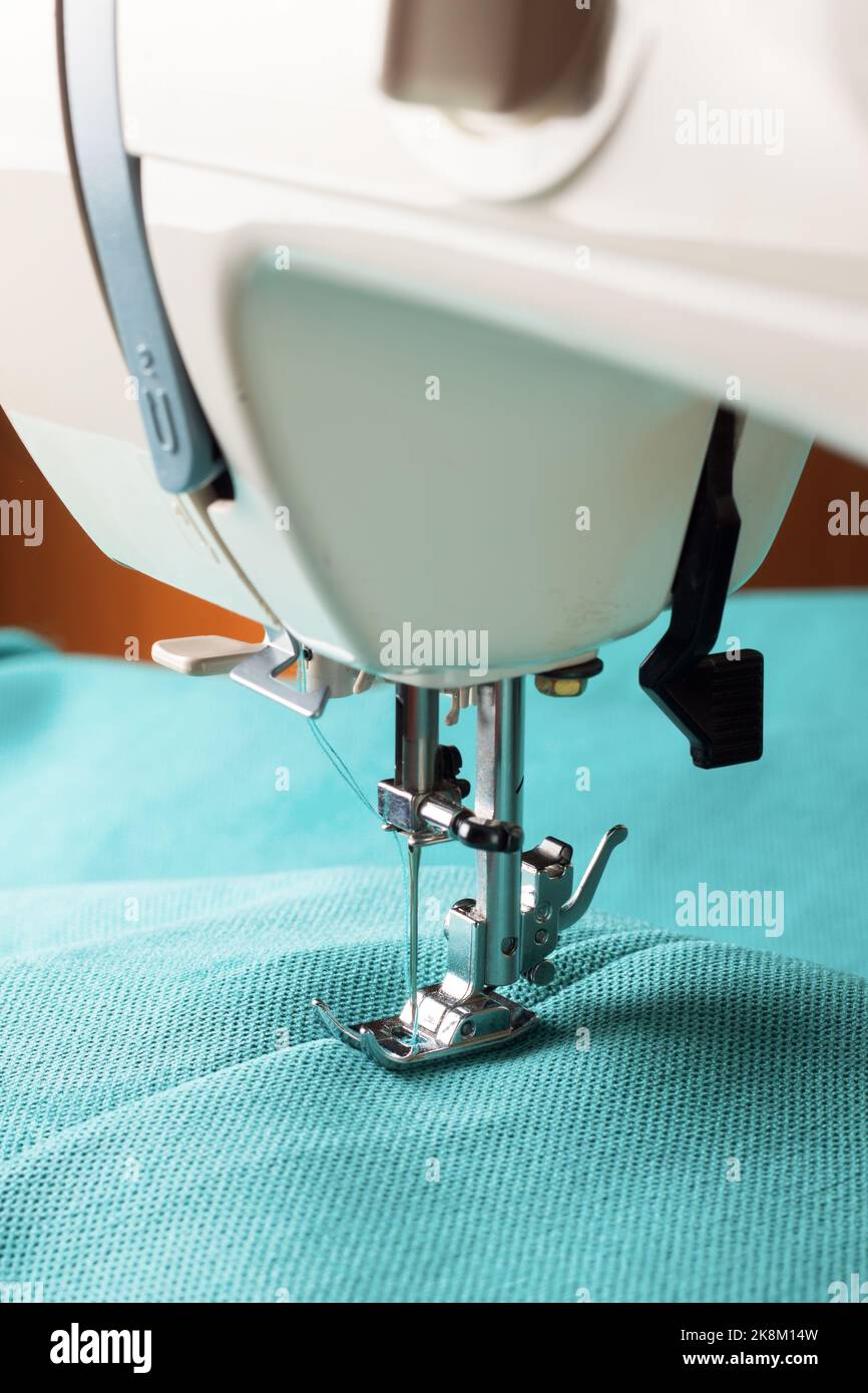 Modern sewing machine working with turquoise fabric. Sewing process. Stock Photo