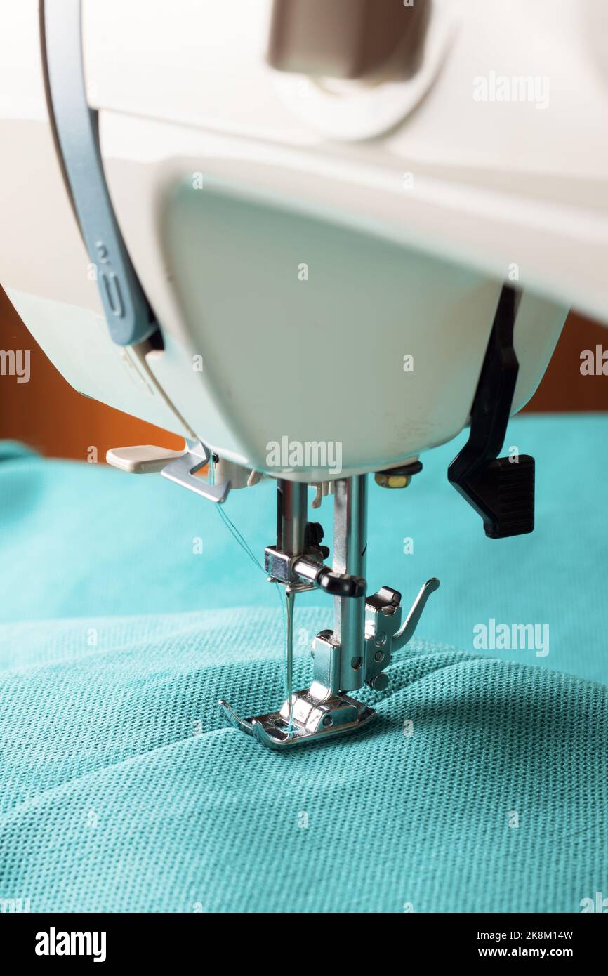 Modern sewing machine working with turquoise fabric. Sewing process