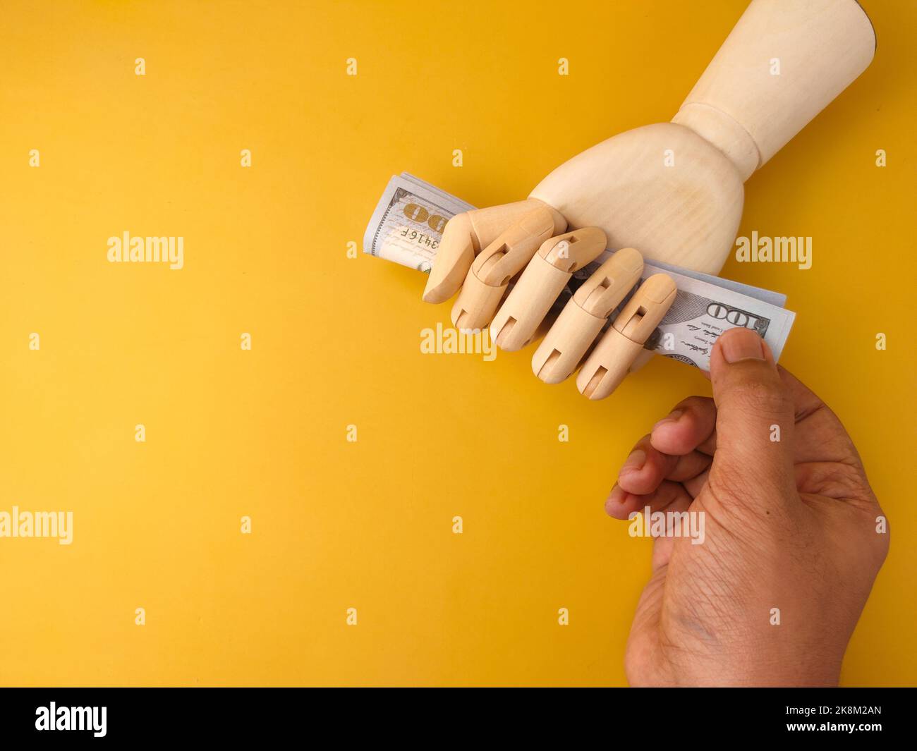 A top view of an adult hand pulling money from a wooden hand grip on a yellow background with copy space Stock Photo