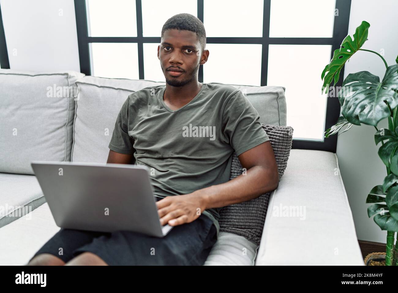 Young african american man using laptop at home sitting on the sofa ...