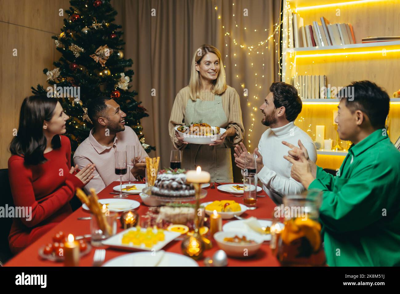 Festive Christmas New Year dinner, various friends celebrate new year together at home, have dinner and drink alcohol at the festive table. Stock Photo