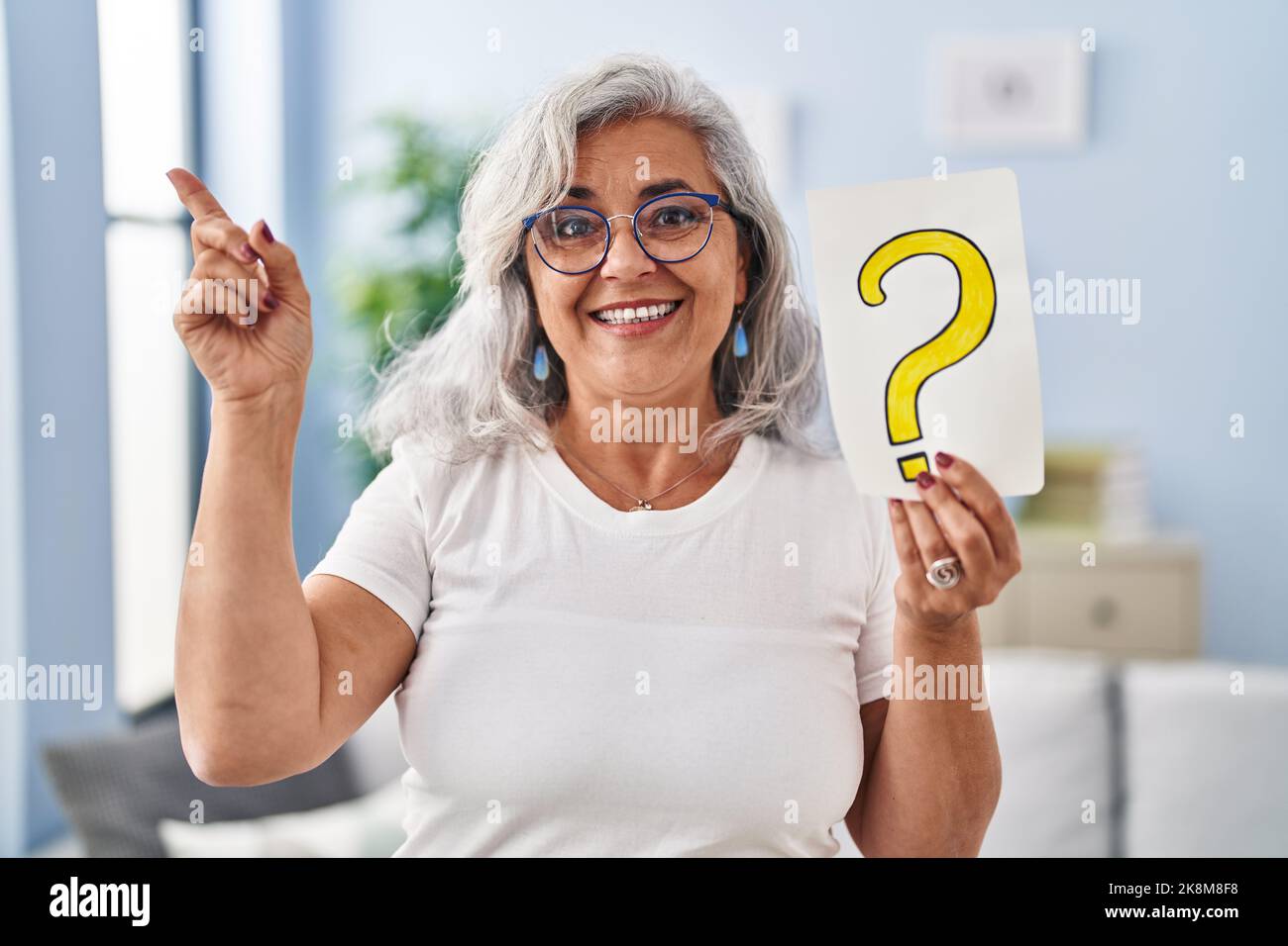 Middle age woman with grey hair holding question mark smiling happy ...