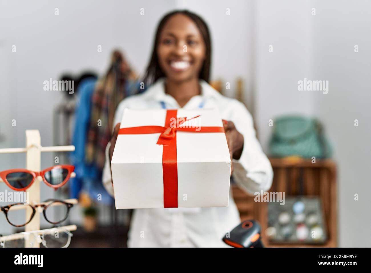 Young african american shopkeeper woman smiling happy holding gift at ...