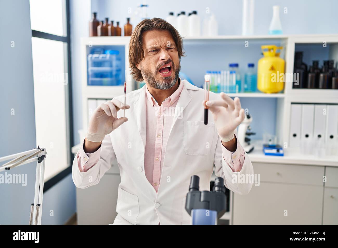 Angry Blood Handsome middle age man holding blood sample at biology laboratory ...