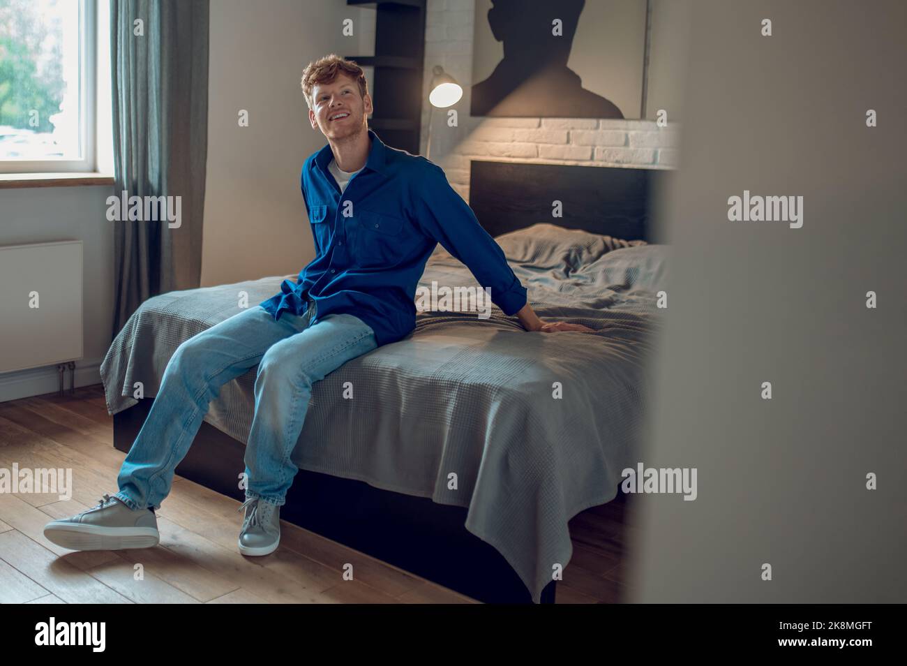 A young man in dark-blue shirt sitting on the bed Stock Photo
