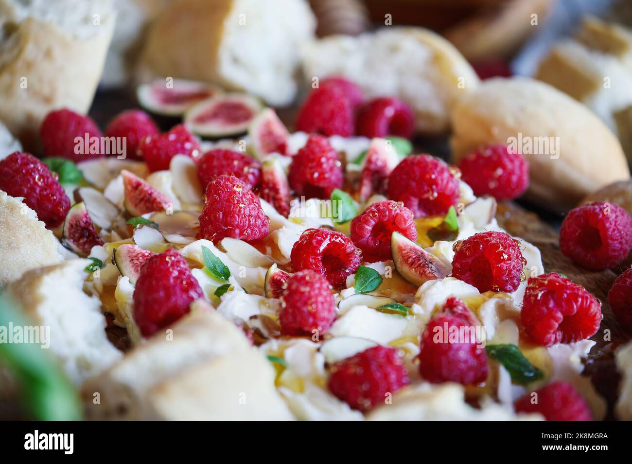 Butter board topped with fresh raspberries, figs, sliced almonds, basil leaves, and drizzled with honey. Selective focus with blurred background. Stock Photo