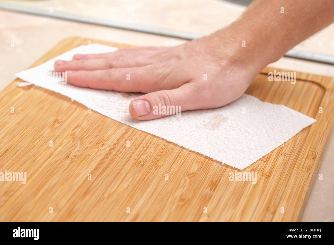 A man wipes a bamboo cutting board with a white paper napkin after