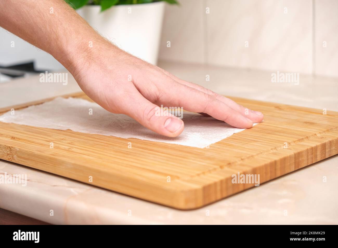 A man wipes a bamboo cutting board with a white paper napkin after