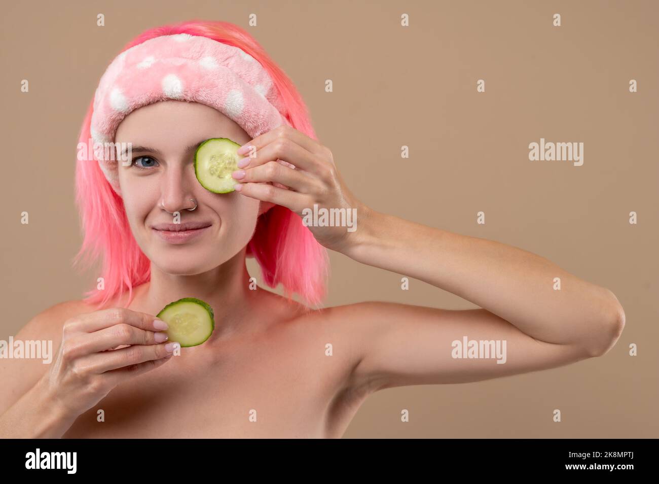 Smiling young girl using cucumber for face care Stock Photo