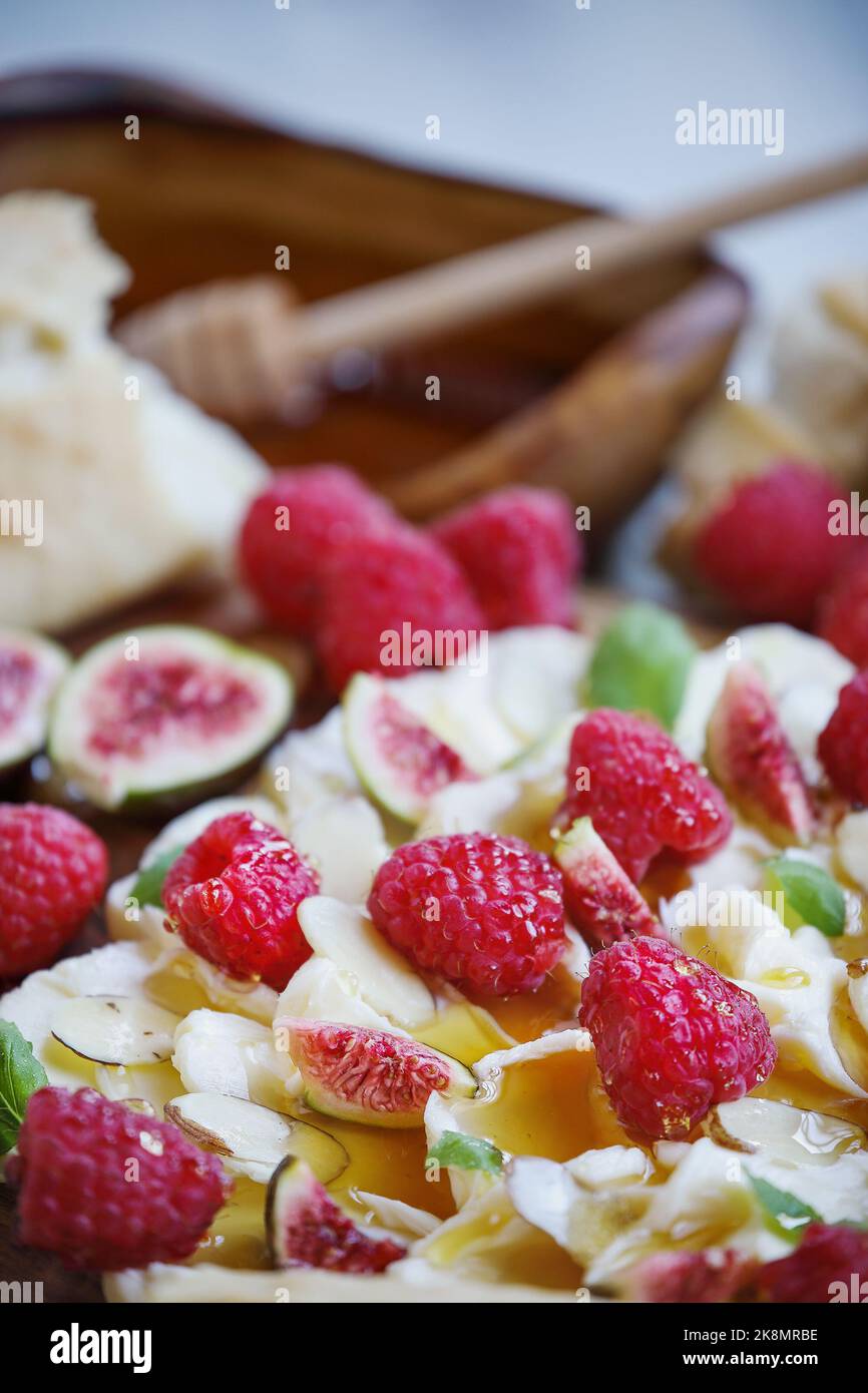 Butter board topped with fresh raspberries, figs, sliced almonds, basil leaves, and drizzled with honey. Selective focus on fig in lower part of image. Stock Photo