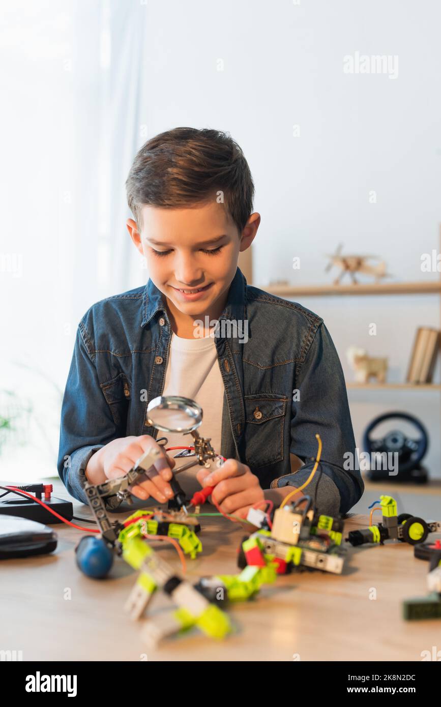 Cheerful boy holding magnifying glass near robotics model at home,stock image Stock Photo