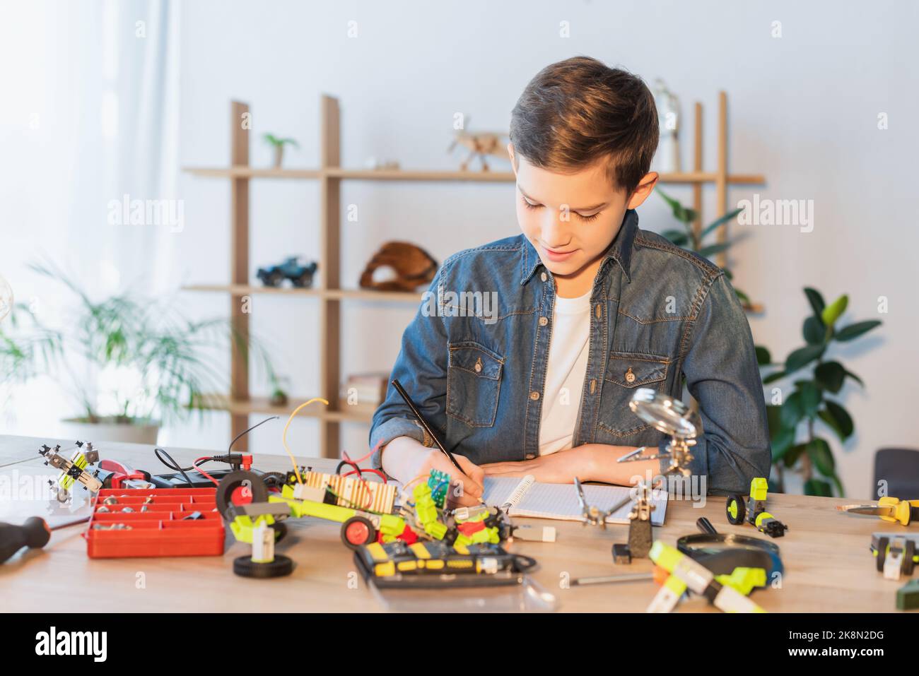 Preteen child writing on notebook near tools and robotic model at home,stock image Stock Photo