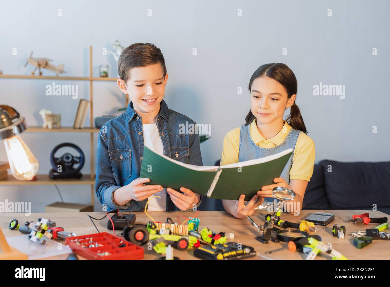 Smiling kids holding notebook near robotic model and tools at home,stock image Stock Photo