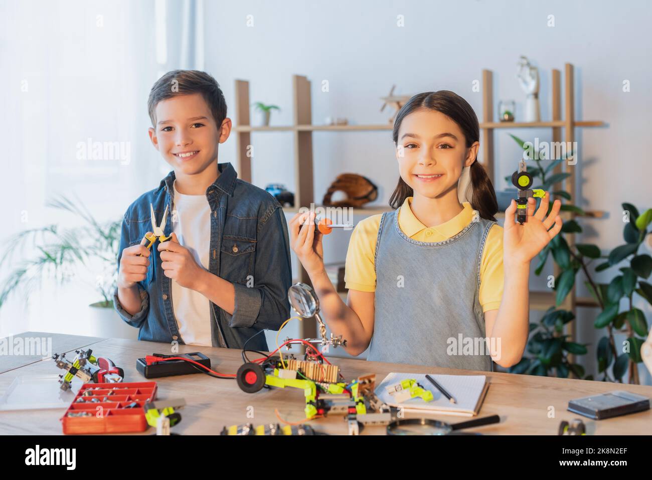 Happy kids holding tools near robotic model on table at home,stock image Stock Photo