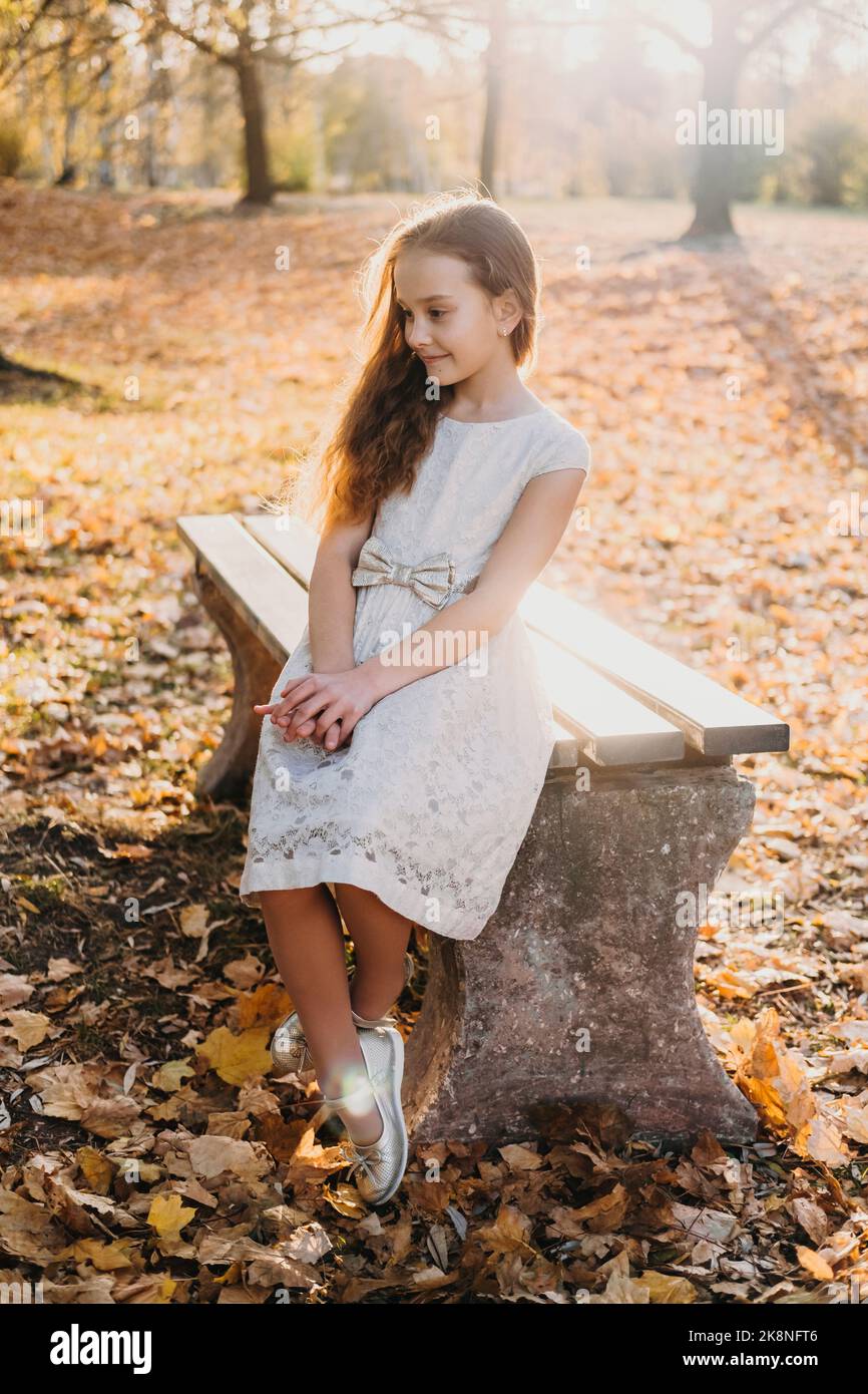 Outdoor portrait of a beautiful little girl in a white dress sitting on ...