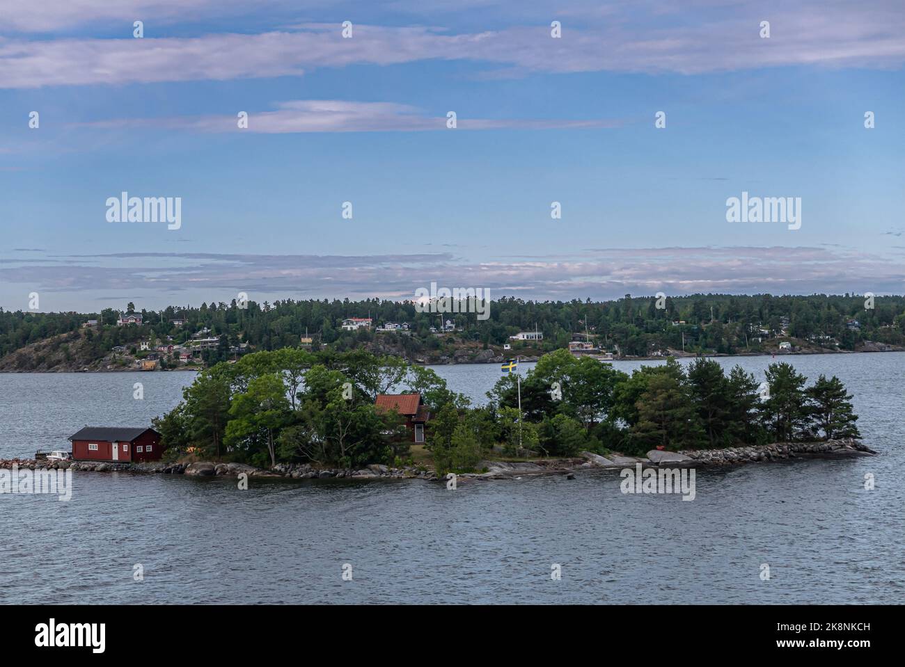 Sweden, Stockholm - July 16, 2022: Morning approach by ship from Baltic. Small Tumlaren Island with a couple buildings and lots of foliage under blue Stock Photo