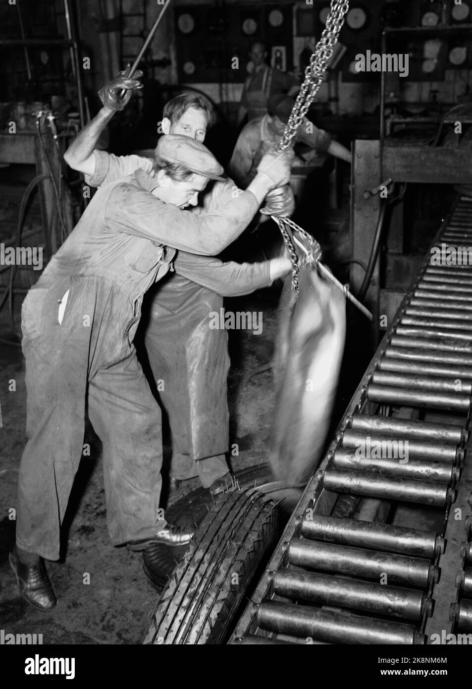 Askim 19471101. Increased production in Askim Rubber Factory. The men produce car tires and women rubber boots. Here we see from the production of car tires. When the car tire is taken out of the large vulcanization boiler, Kristian Hansen and Einar Fager pull over it and remove the 'air dun' that has secured the tire against being squeezed together. Photo: Th. Skotaam Altuell / NTB Stock Photo