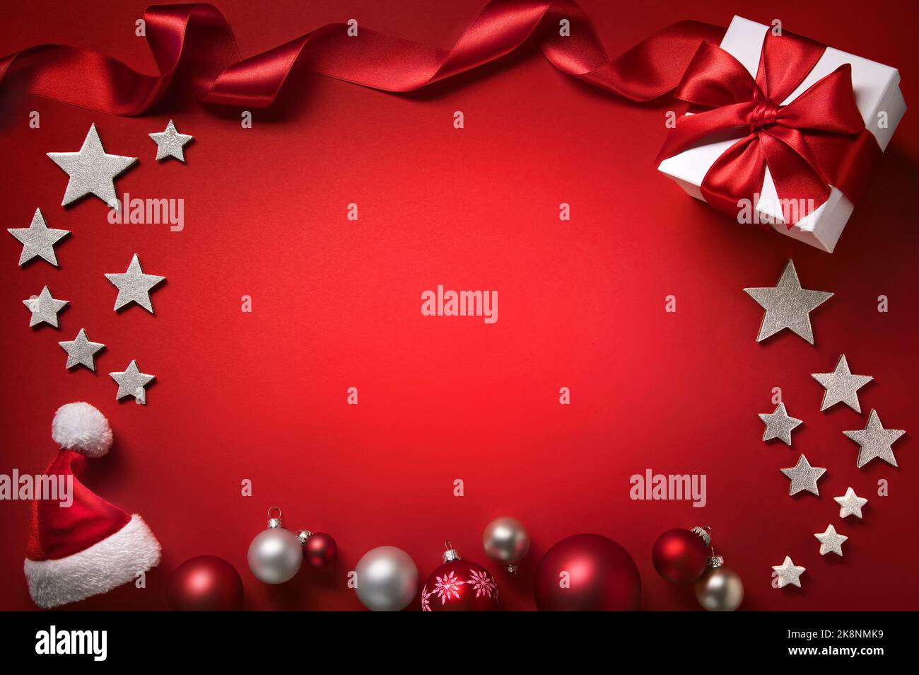 Christmas background in red, with a frame composed of baubles, gift box, stars, ribbon and hat, free illuminated copy space Stock Photo