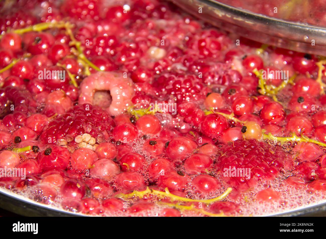 Compote with raspberries and red polachek is boiling. Hot compote with mix from berry. Stock Photo