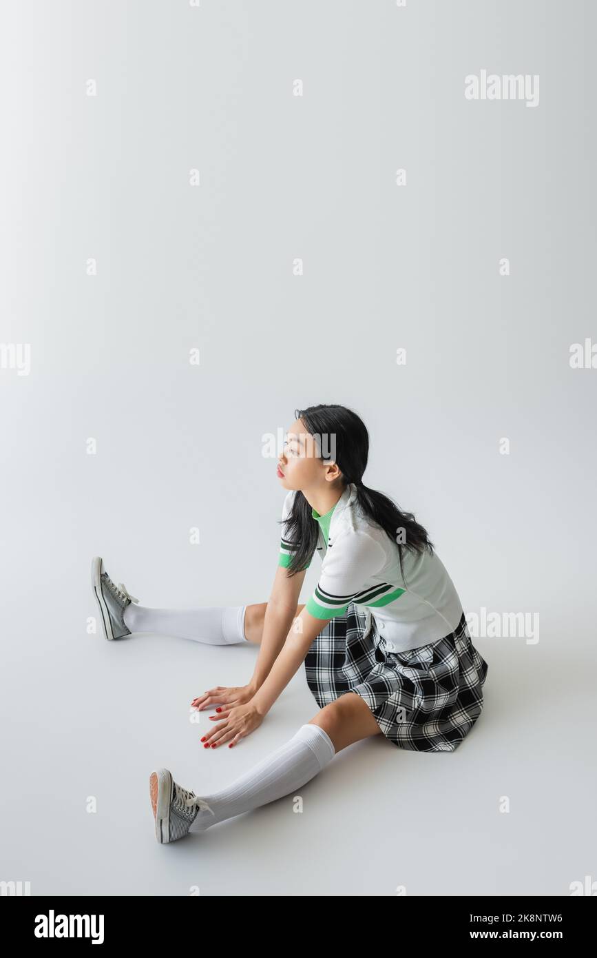 Stylish asian woman in skirt and knee socks sitting on grey background Stock Photo