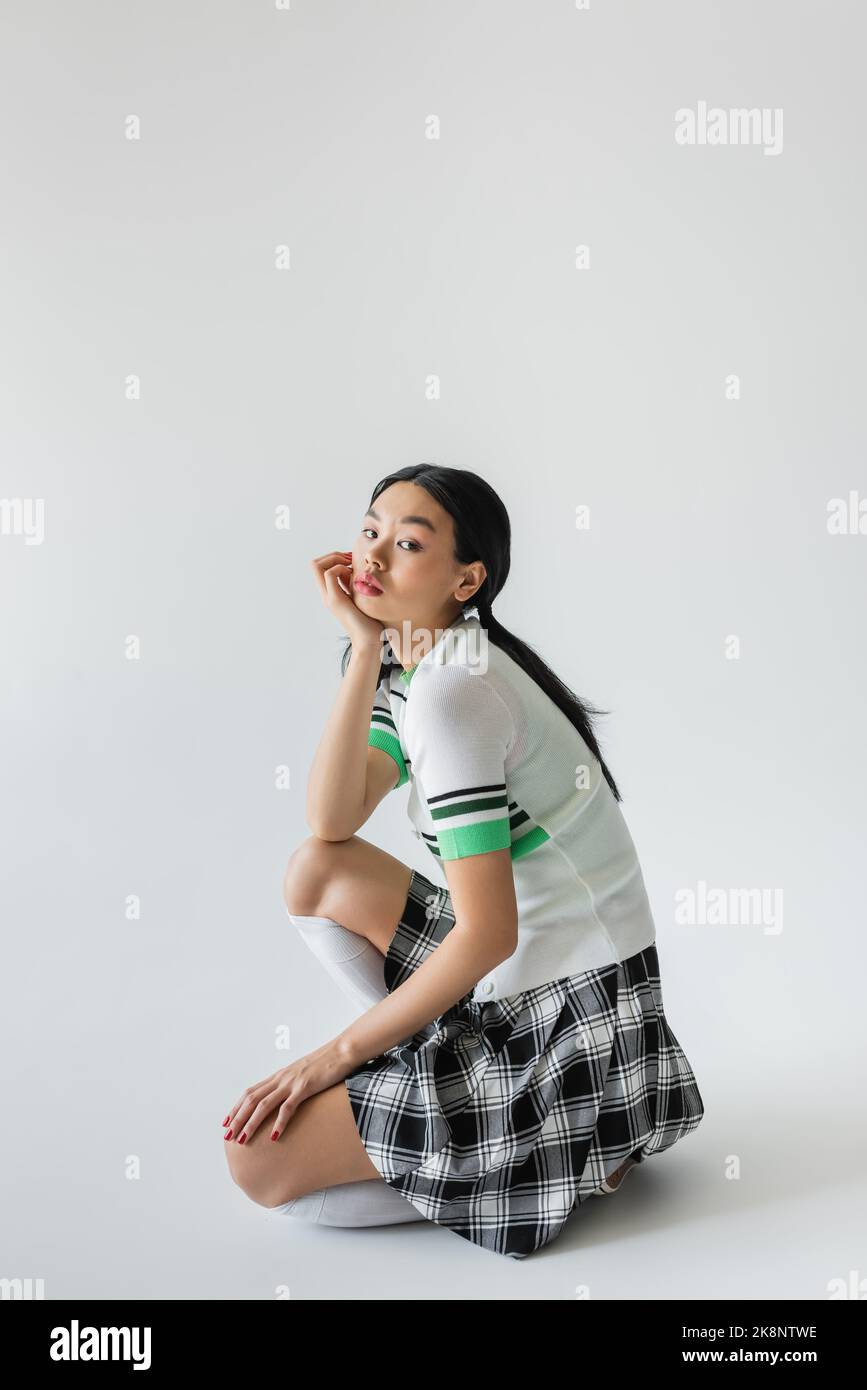 Young asian woman in checkered skirt and knee socks posing on grey background Stock Photo