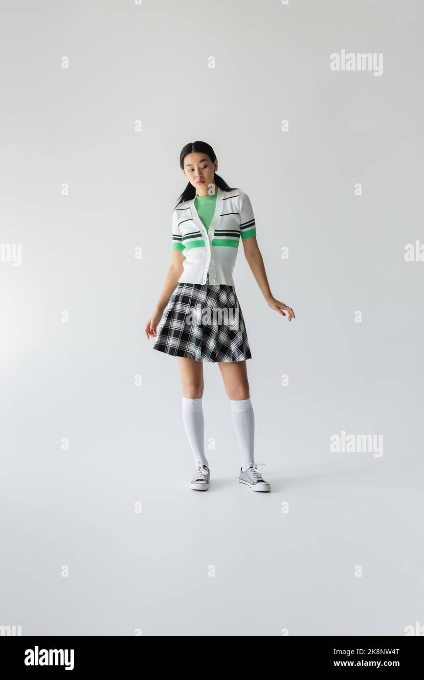 Full length of young asian woman in skirt and knee socks standing on grey background Stock Photo