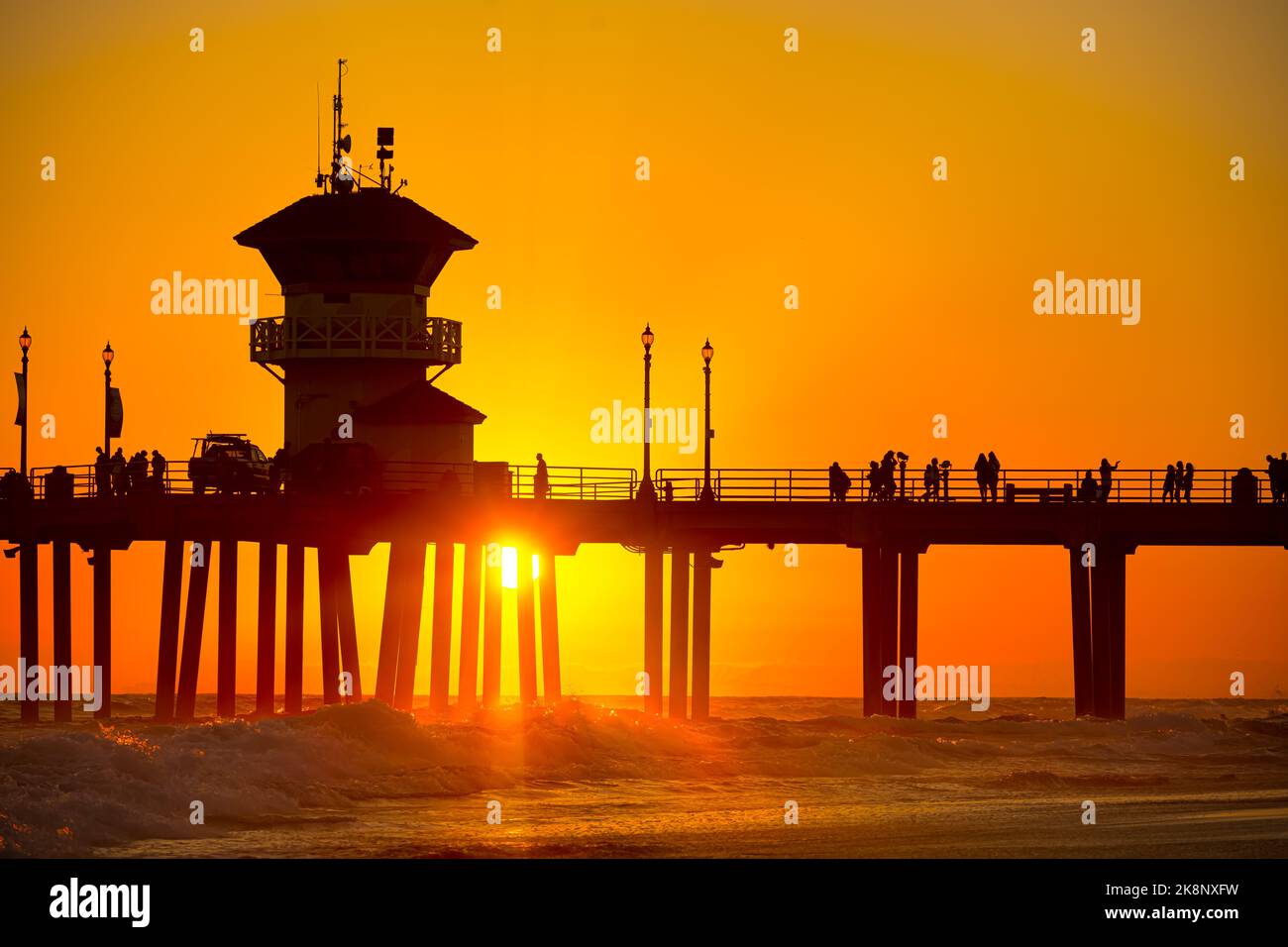 A silhouette of a pier with walking people under an orange sunset sky on Huntington Beach, California Stock Photo