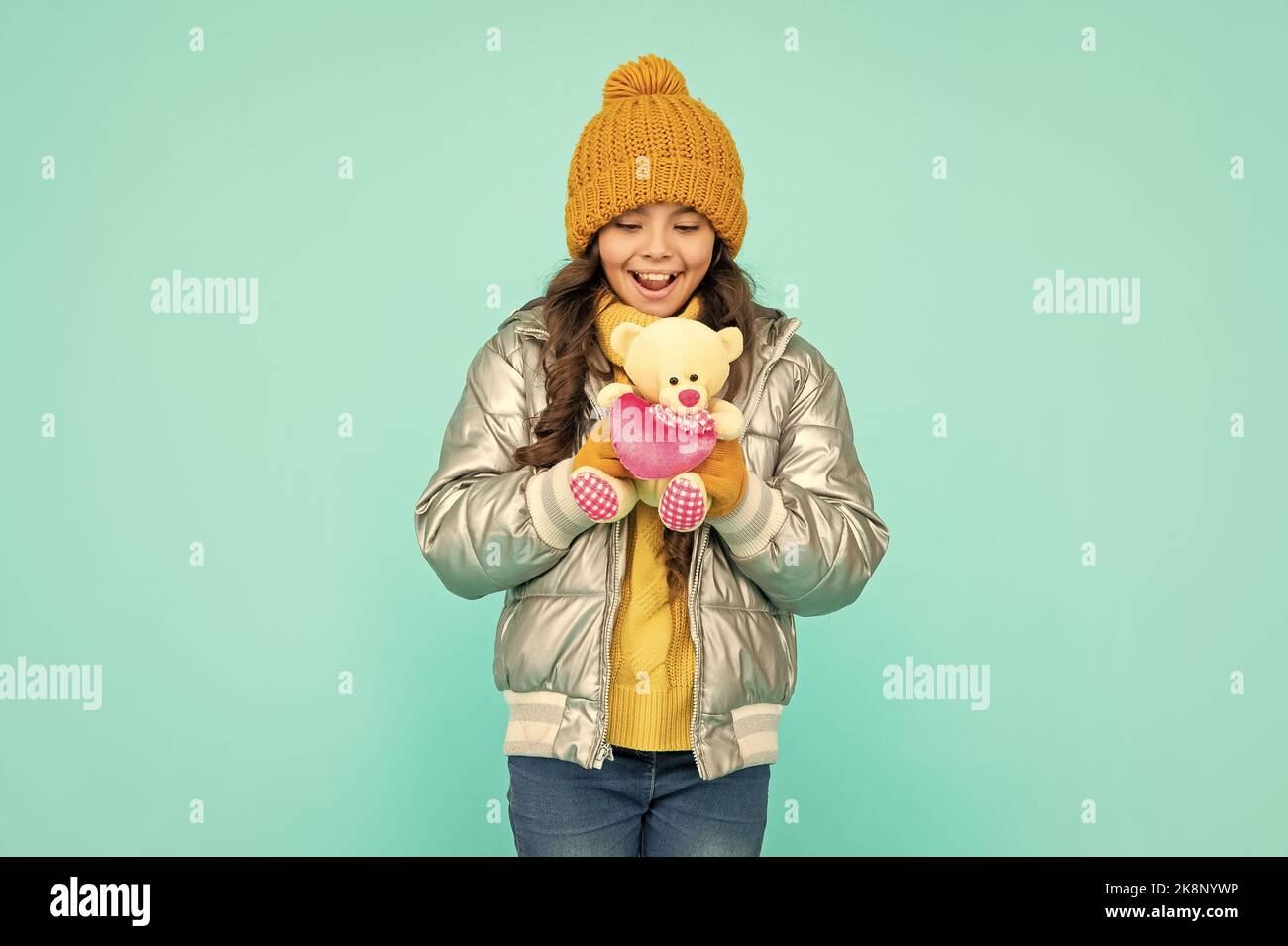 amazed child in hat and puffer jacket with toy on blue background, valentines day Stock Photo