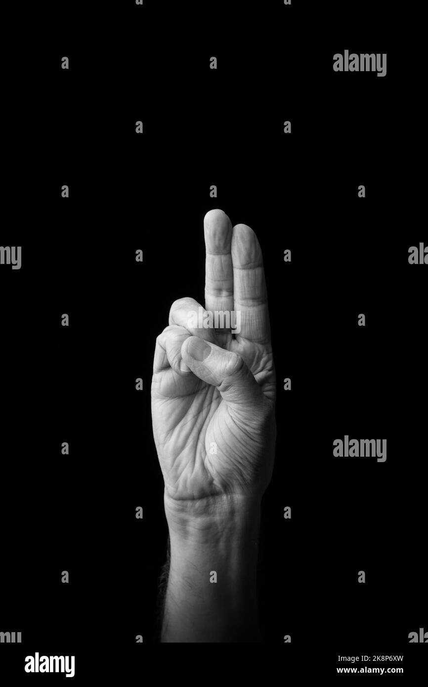 Dramatic black and white image of a male hand fingerspelling the Japanese sign language letter 'U' or 'ぅ', against a dark background with copy space Stock Photo