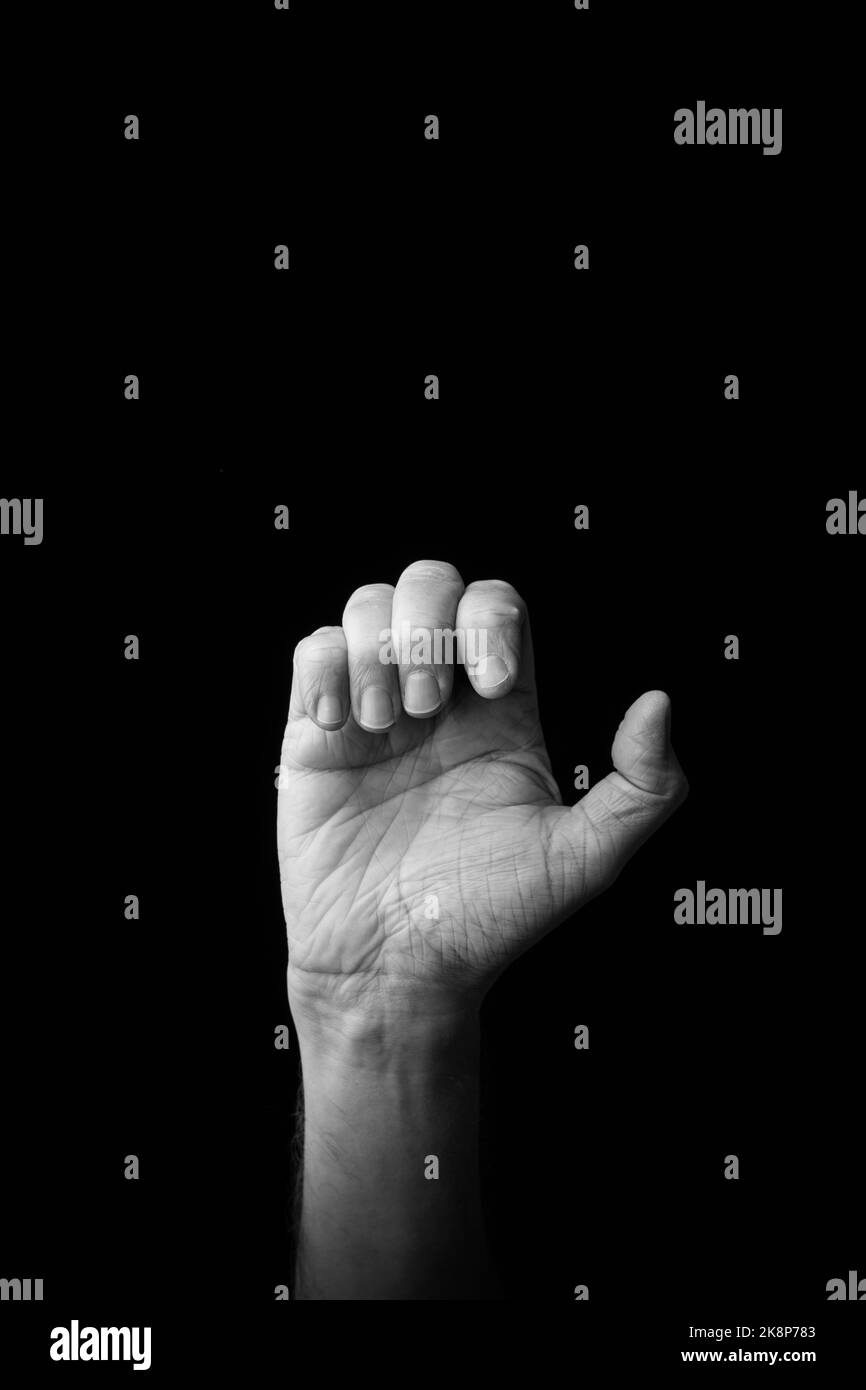 Dramatic black and white image of a male hand fingerspelling the Japanese sign language letter 'E' or 'ぇ', against a dark background with copy space Stock Photo