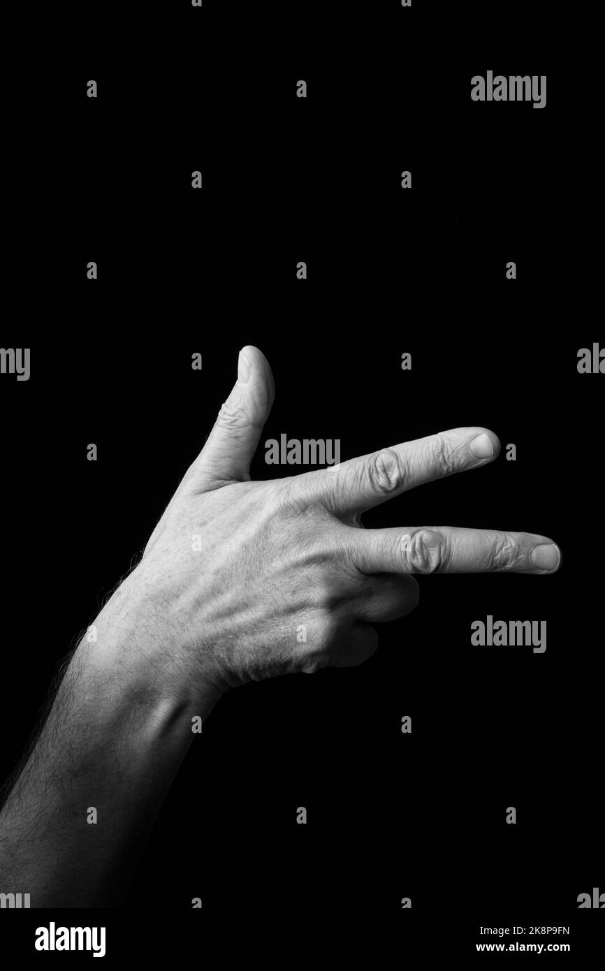 Dramatic black and white image of a male hand fingerspelling the Japanese sign language letter 'SHI' or 'し', against a dark background with copy space Stock Photo