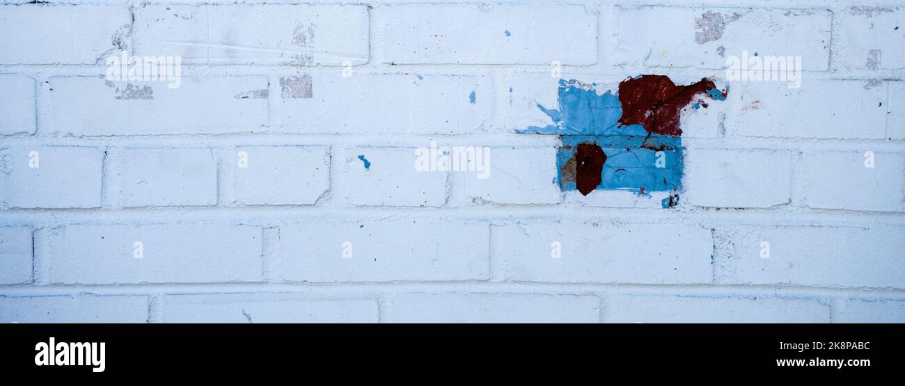 Old brick wall painted white with blue and red geometric squares. Stock Photo