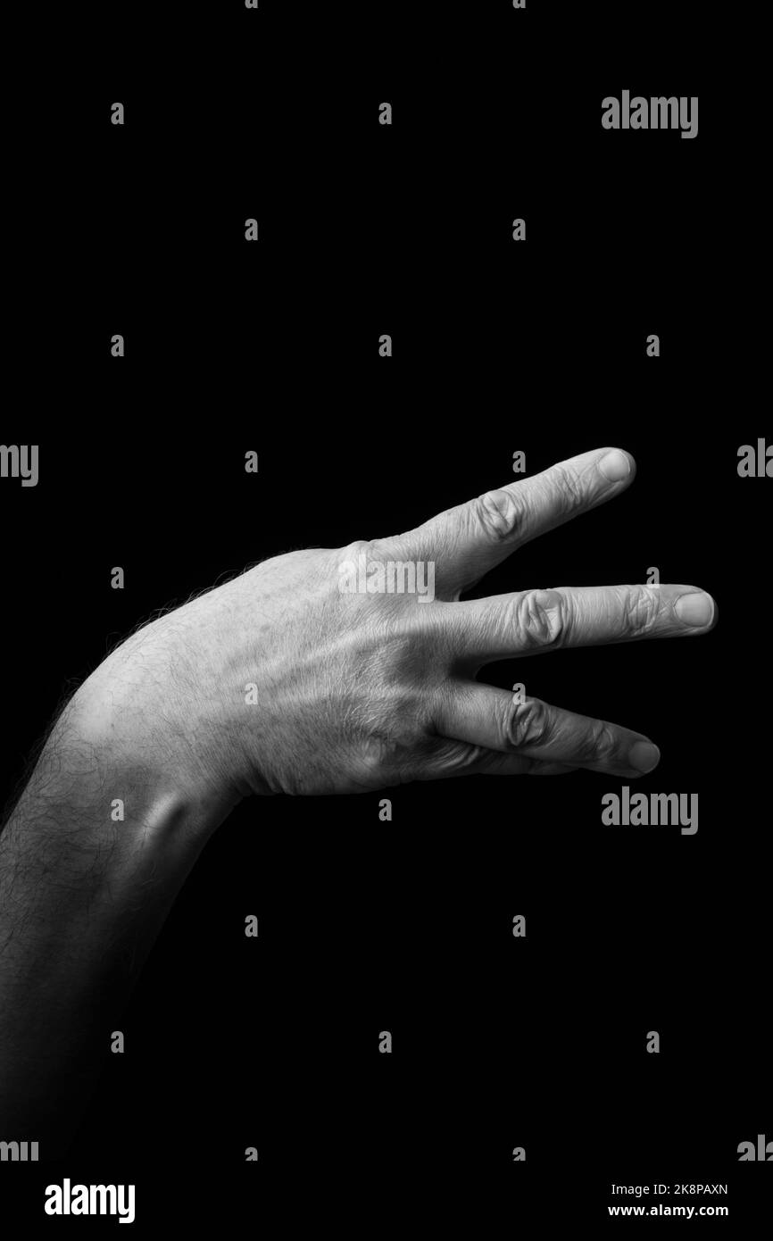 Dramatic black and white image of a male hand fingerspelling the Japanese sign language letter 'MI' or 'み', against a dark background with copy space Stock Photo