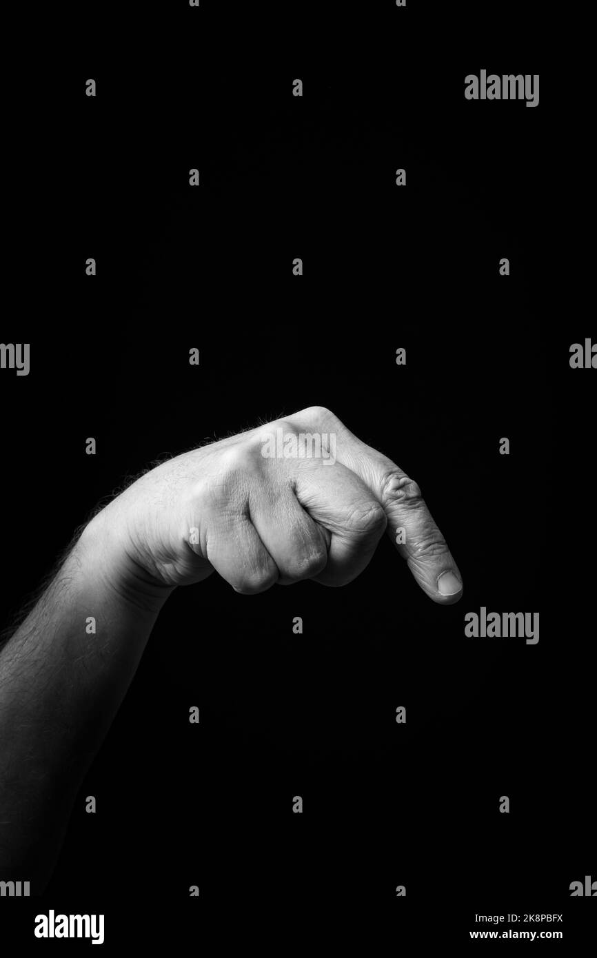 Dramatic black and white  image of a male hand fingerspelling the Japanese sign language letter 'SO' or 'そ', against a dark background with copy space Stock Photo