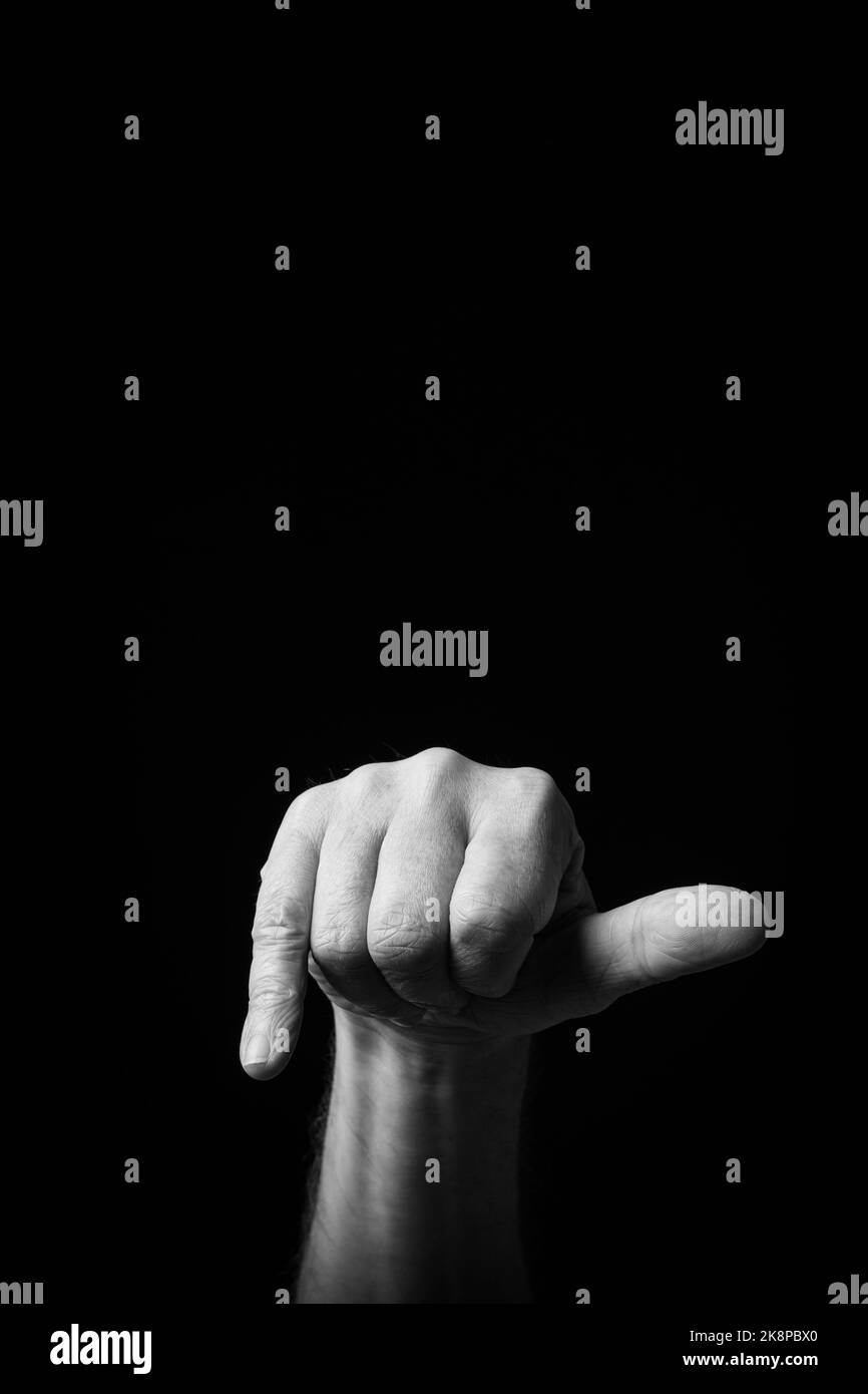 Dramatic black and white  image of a male hand fingerspelling the Japanese sign language letter 'HE' or 'へ', against a dark background with copy space Stock Photo
