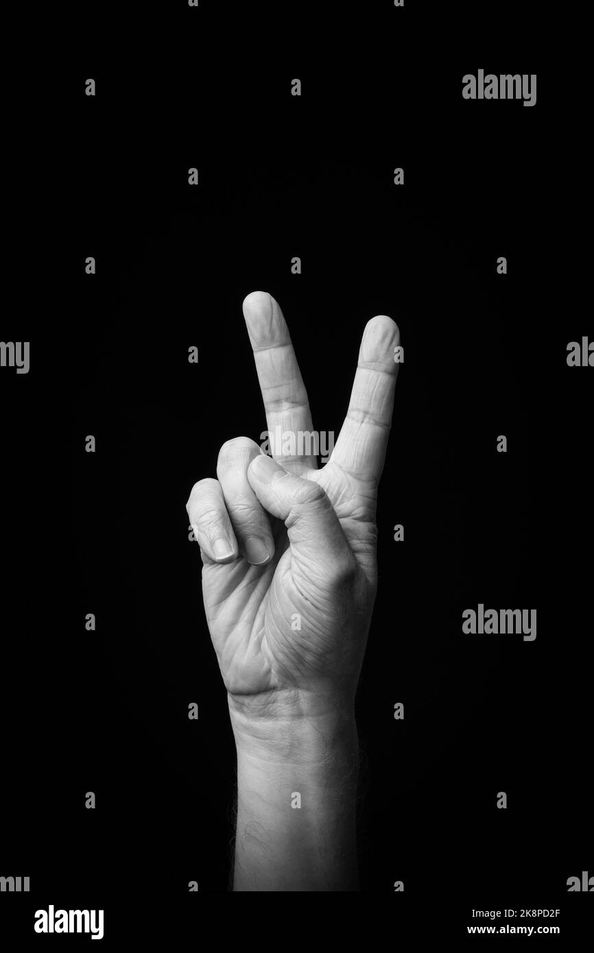 Dramatic black and white  image of a male hand fingerspelling the Japanese sign language letter 'KA' or 'か', against a dark background with copy space Stock Photo